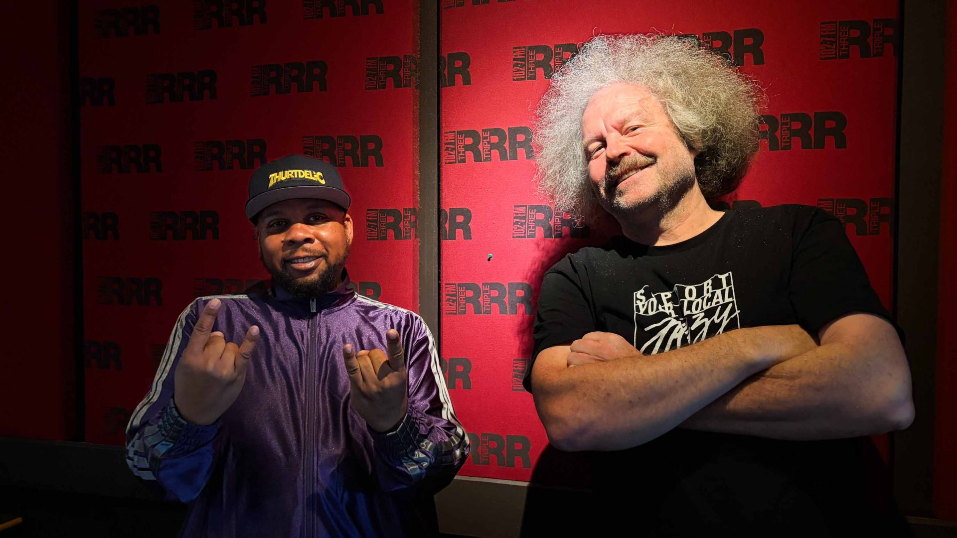 Two men smile in front of a red media wall.