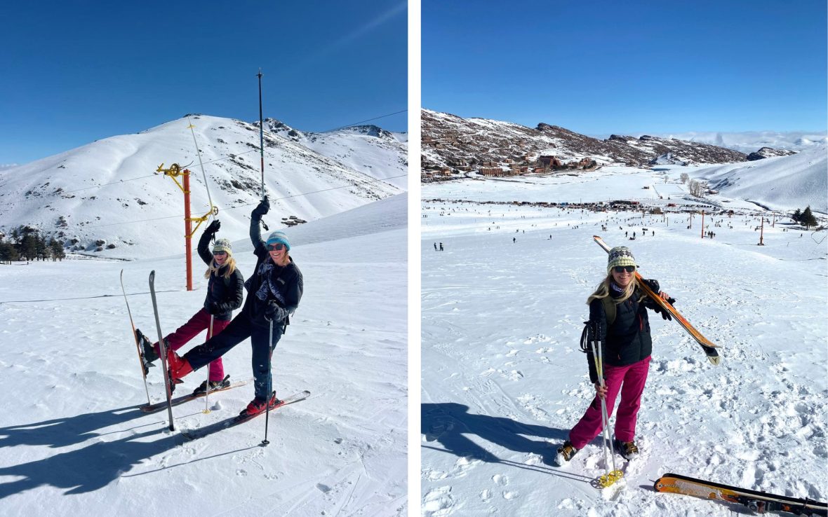 Two women wearing skis smile for a photo.