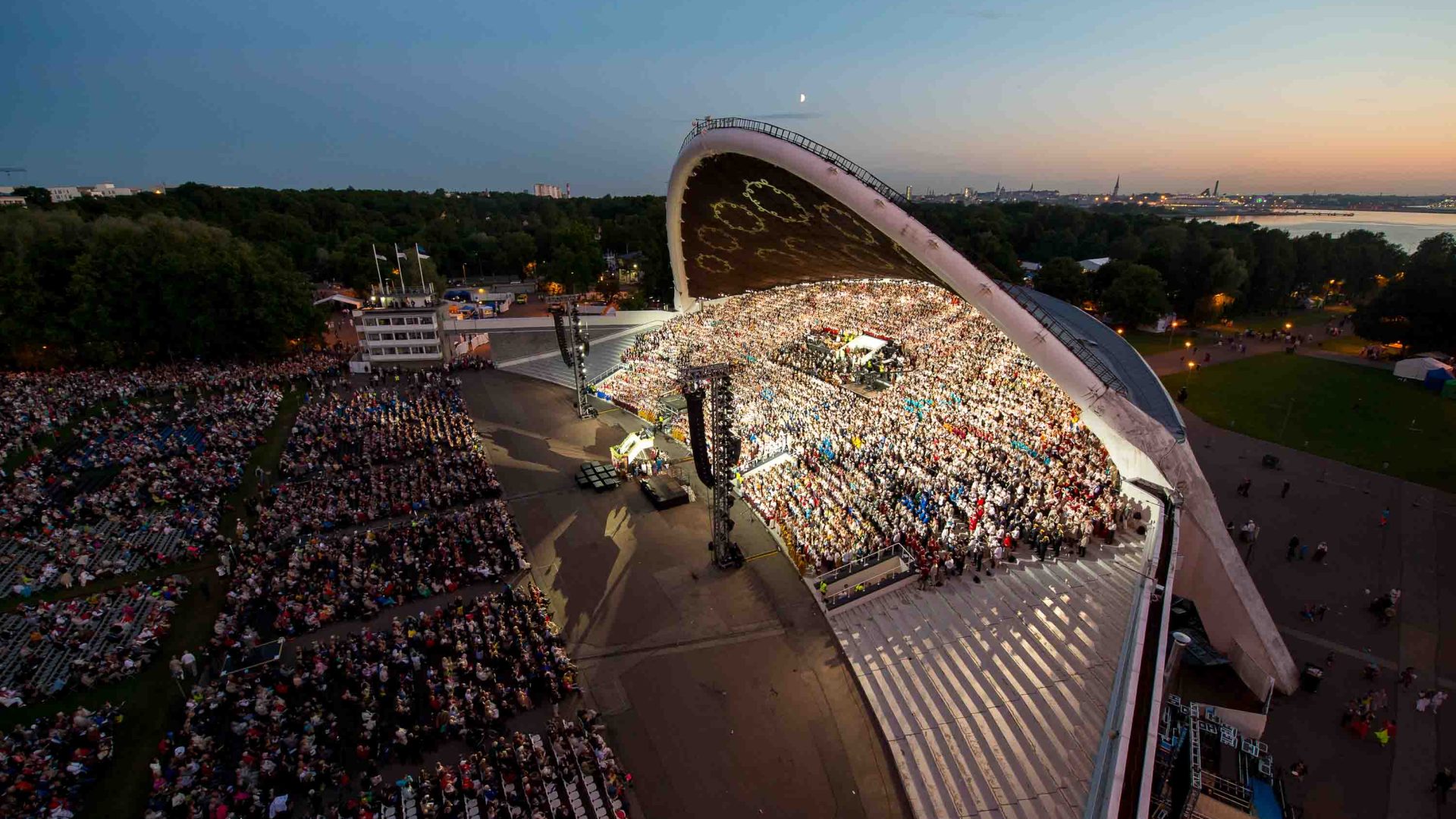 A stadium lit up at night is filled with thousands of people singing.