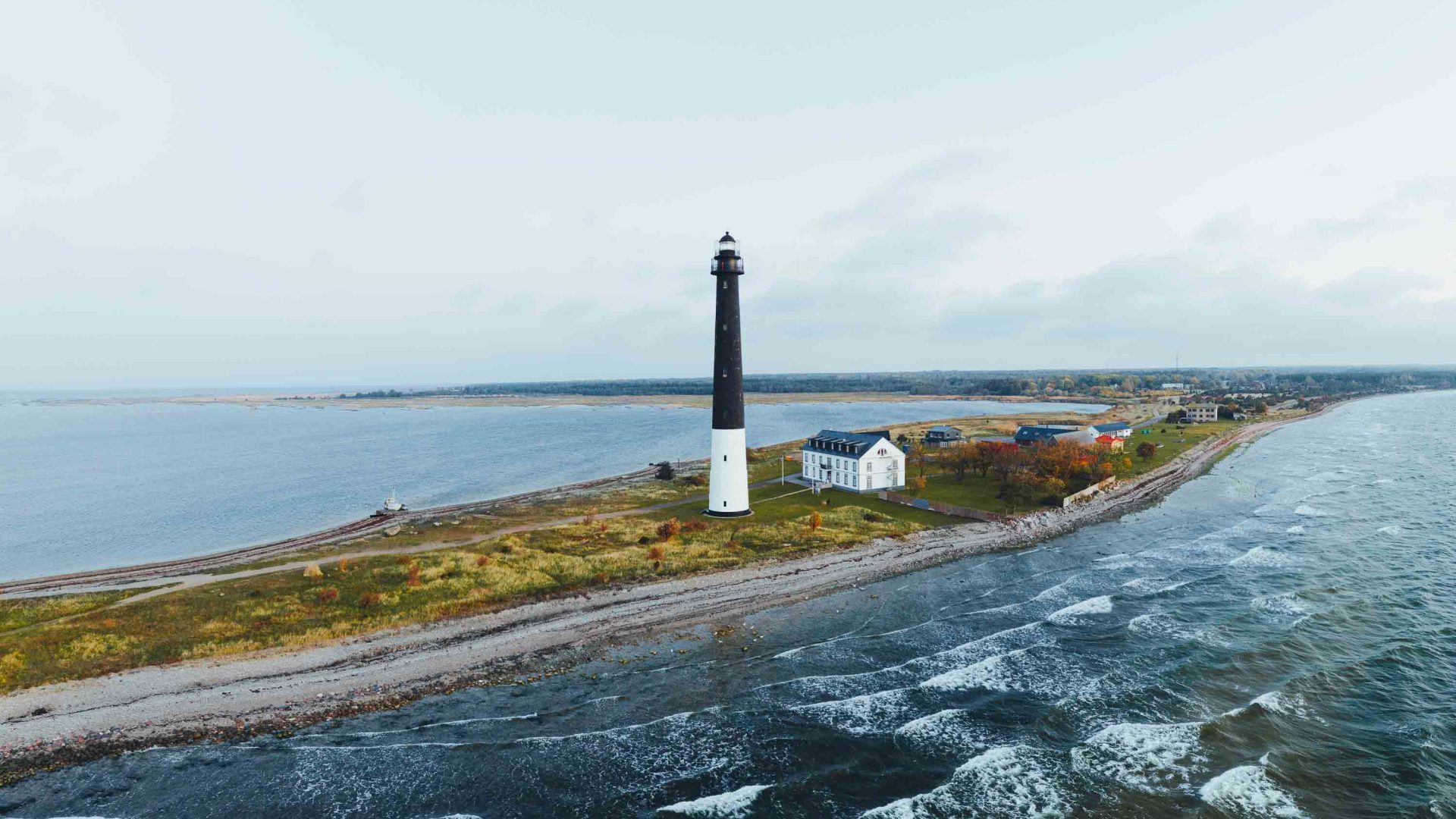 A black and white lighthouse stands on a narrow strip of land.