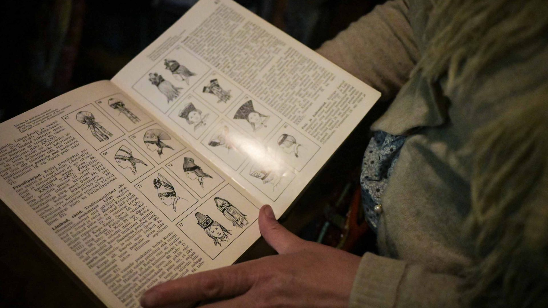 A womans hands holds a book open to pages of head pieces from different regions of Estonia.