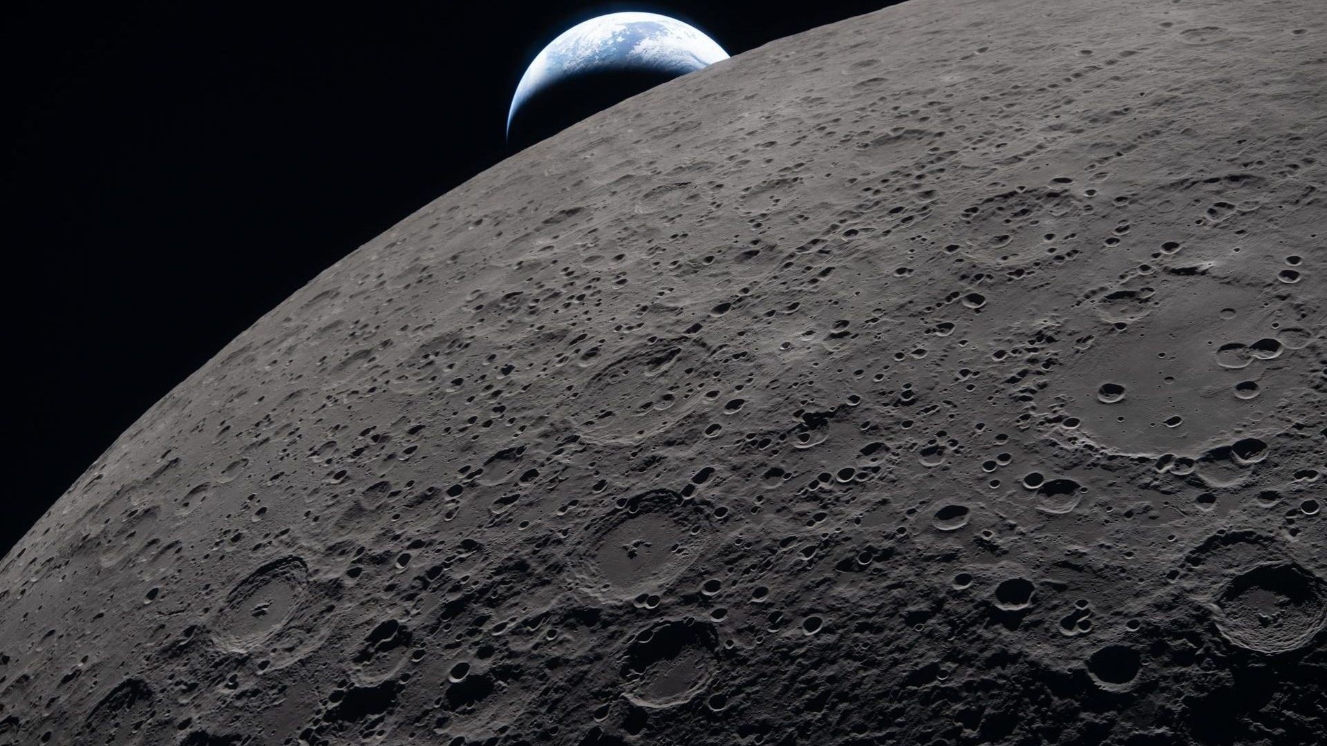 The lunar surface fills the frame in sharp detail, as seen during the Artemis II lunar flyby, while a distant Earth sets in the background. This image was captured at 6:41 p.m. EDT, on April 6, 2026, just three minutes before the Orion spacecraft and its crew went behind the Moon and lost contact with Earth for 40 minutes before emerging on the other side. In this image, the dark portion of Earth is experiencing nighttime, while on its day side, swirling clouds are visible over the Australia and Oceania region. In the foreground, Ohm crater shows terraced edges and a relatively flat floor marked by central peaks — formed when the surface rebounded upward during the impact that created the crater.