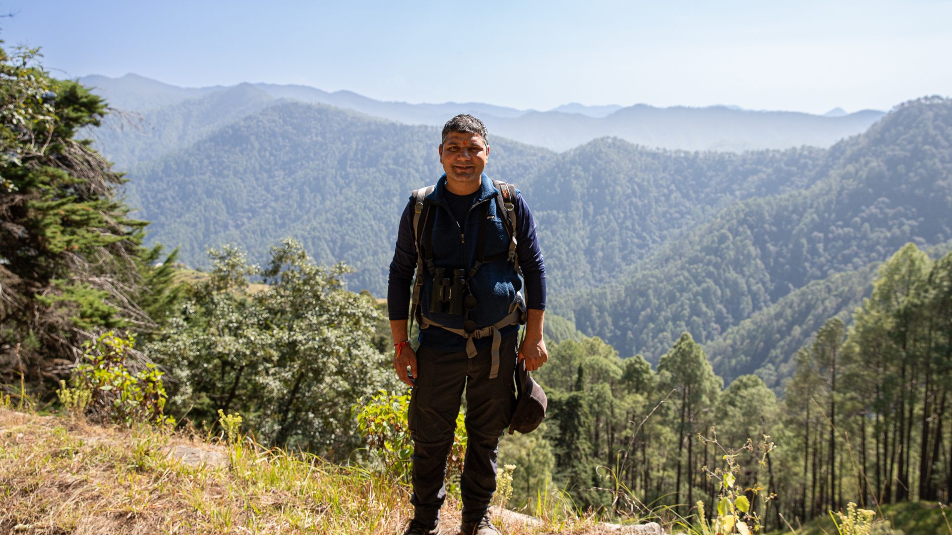 A man stands in front of mountains and smiles.