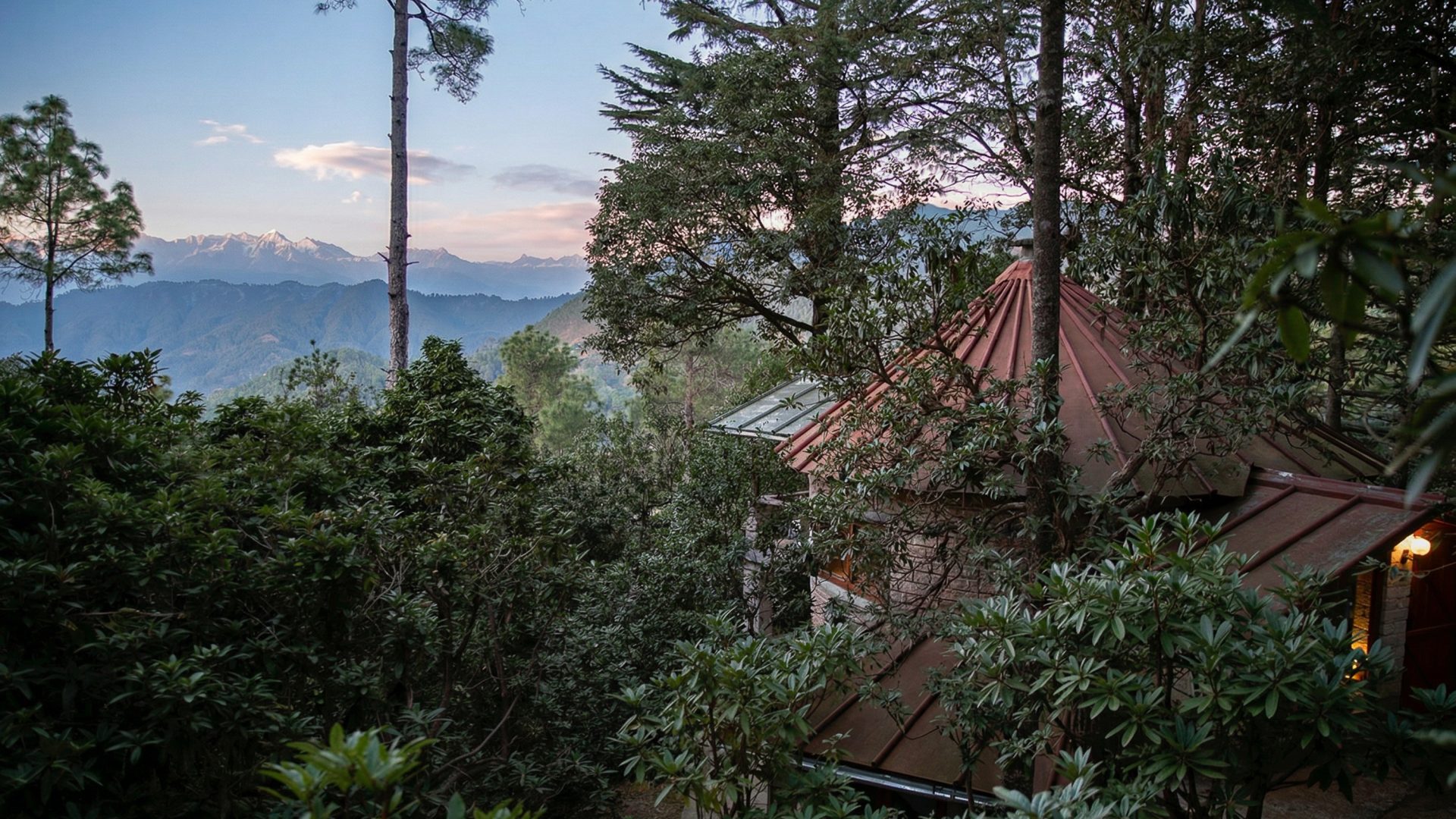 A stone cottage nestled in the trees looks out over mountains.