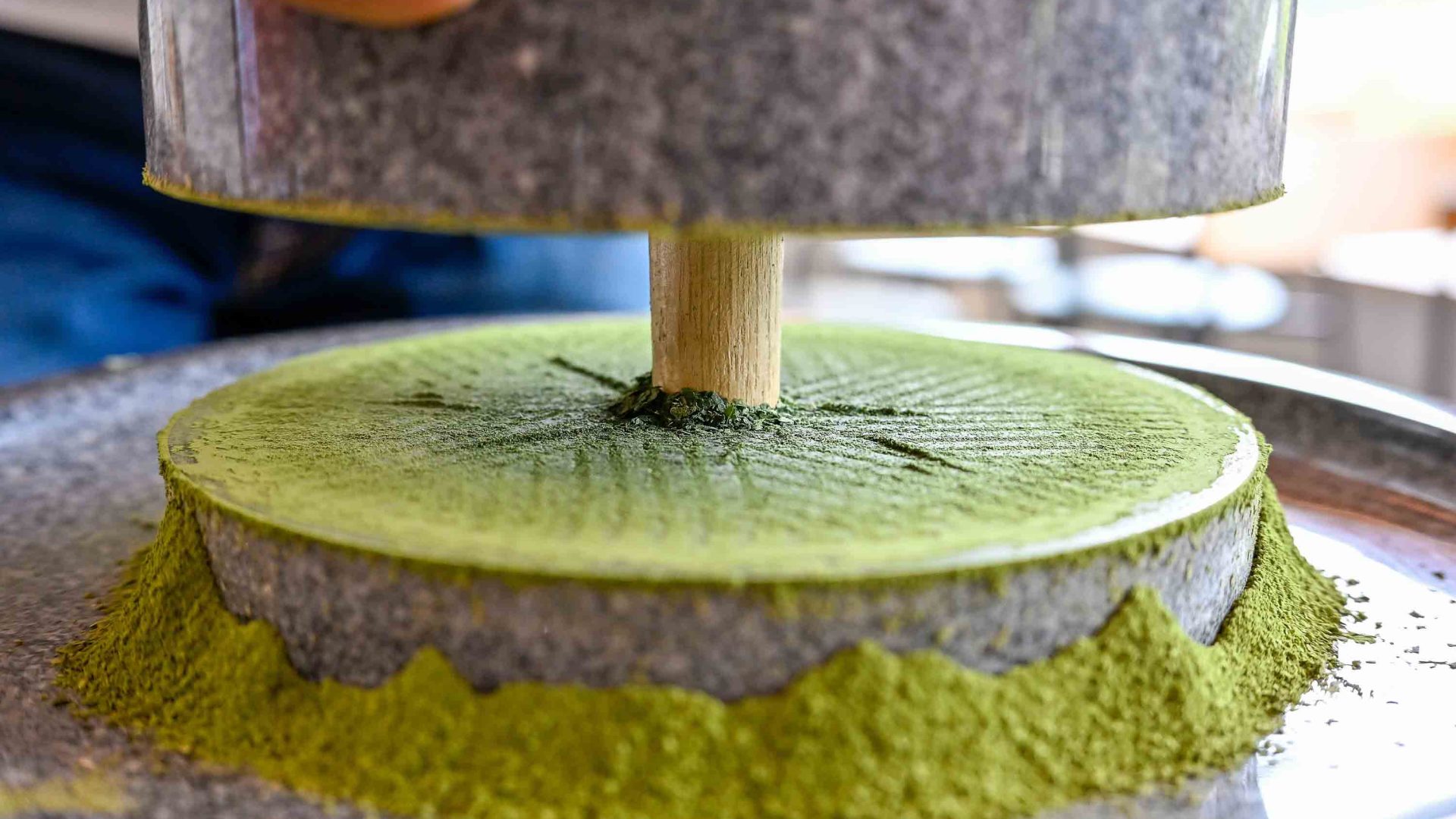 A stone mill grinding leaves into a fine green powder.