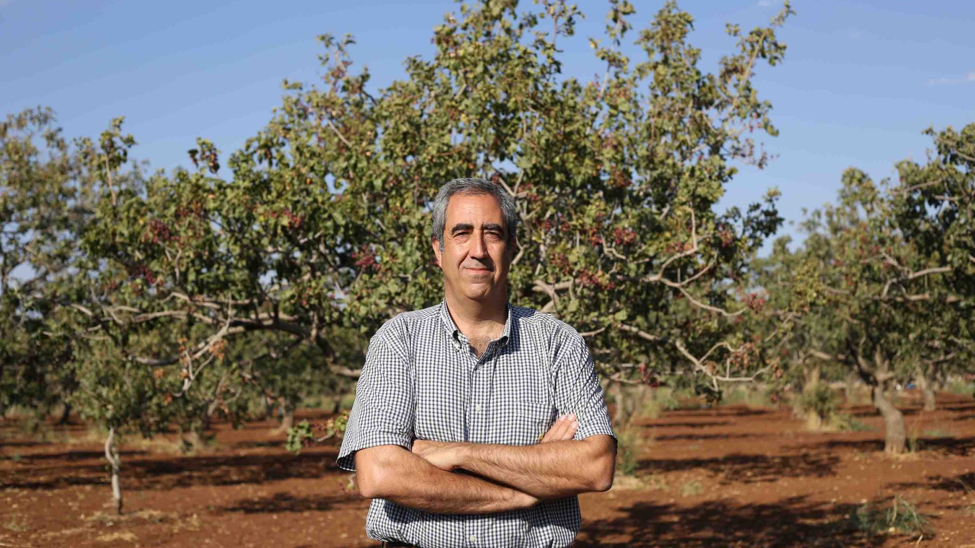 A man stands with his arms crossed in front of a farm.