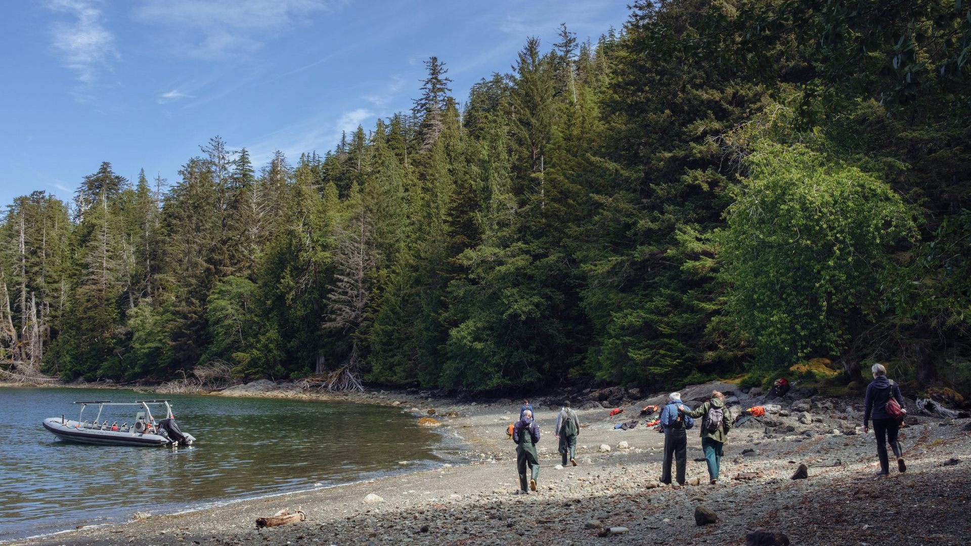 People walk along shore to zodiac boat