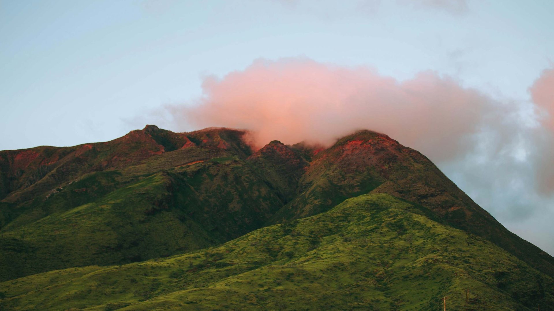 An orange cloud sits on top of a lush green mountain.