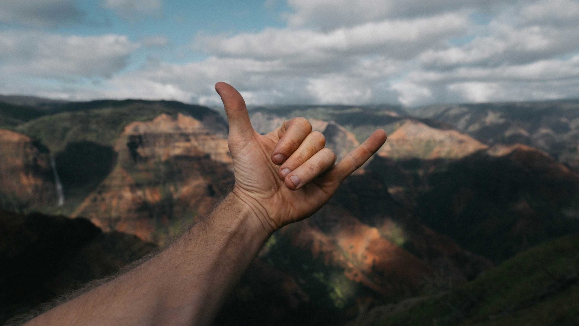 A hand does the Shaka sign in front of a canyon.