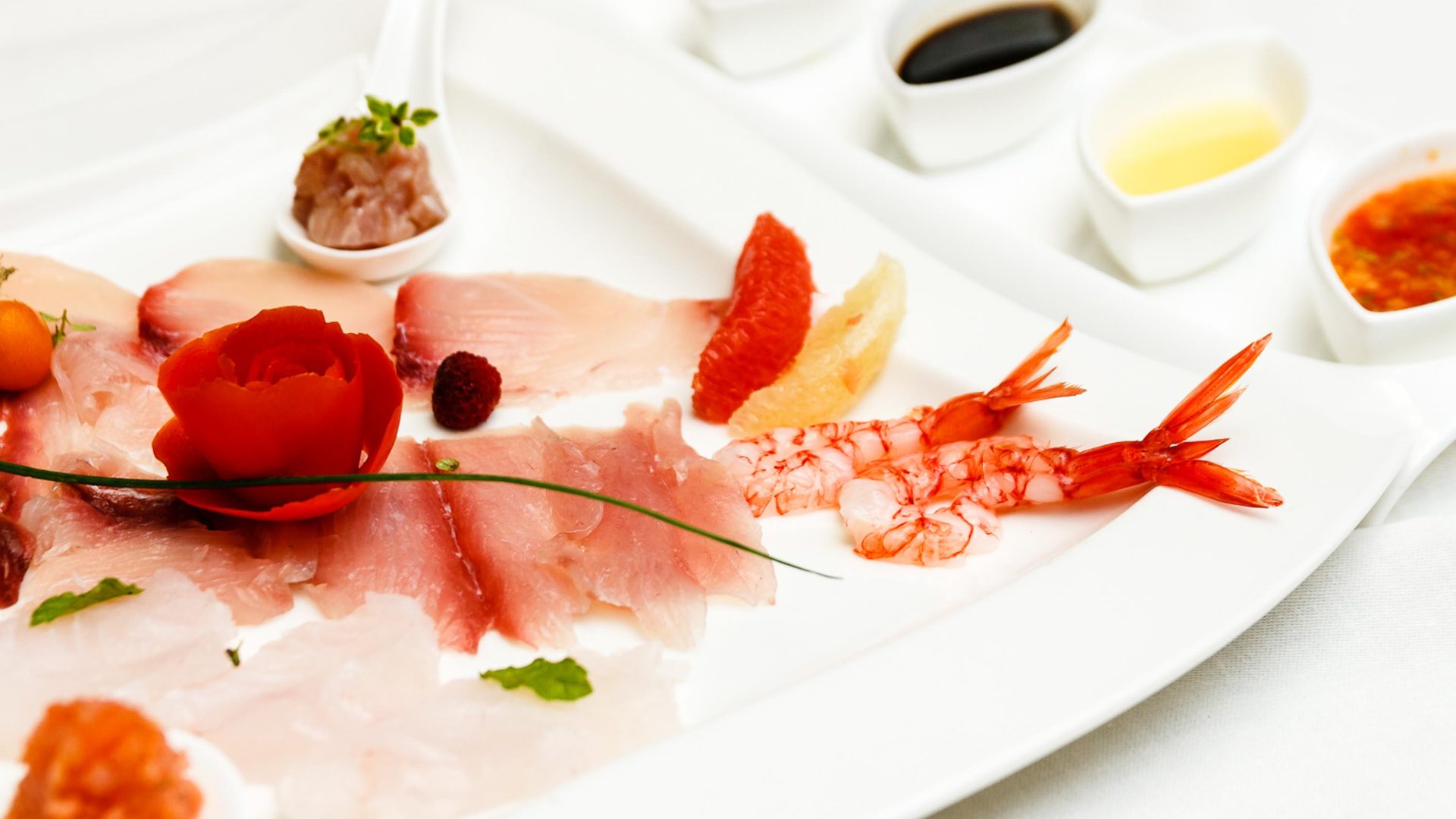 A plate of raw seafood carefully sliced and prepared with dipping sauces.