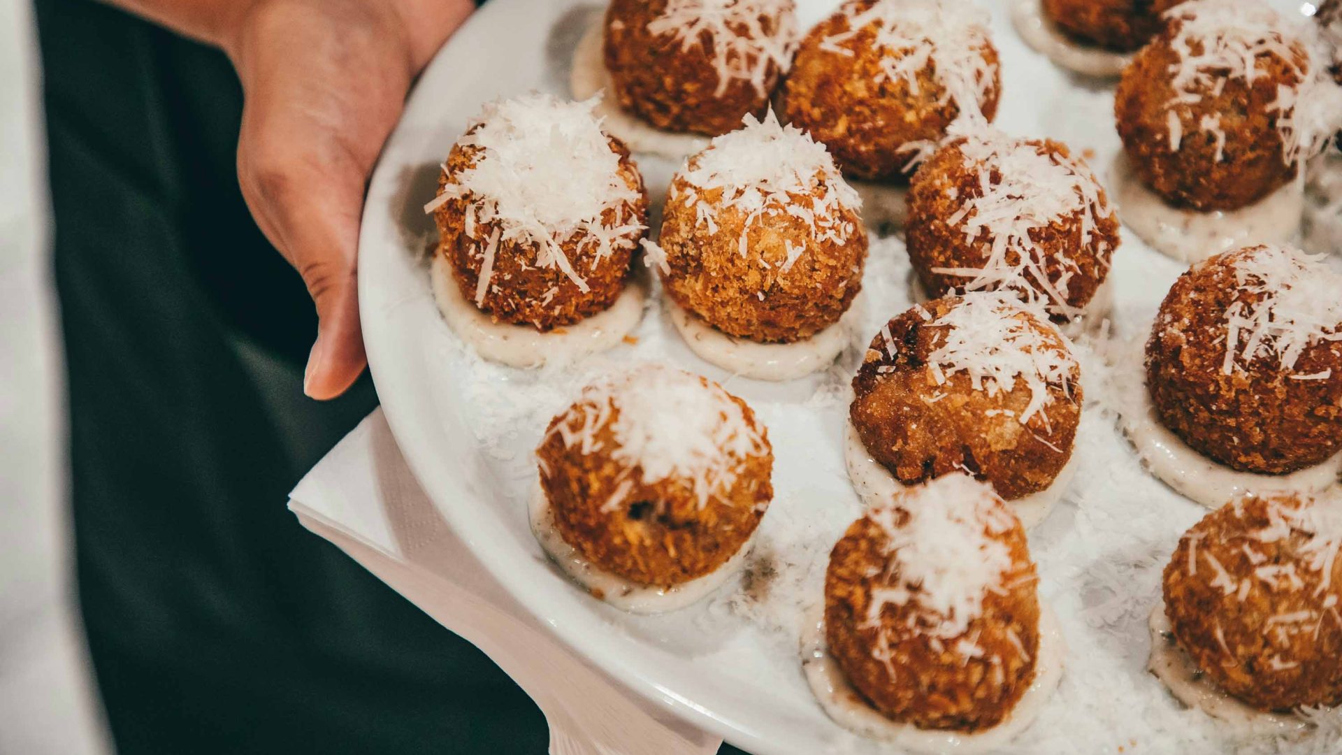 Hands hold a plate of arancini balls with cheese on them.