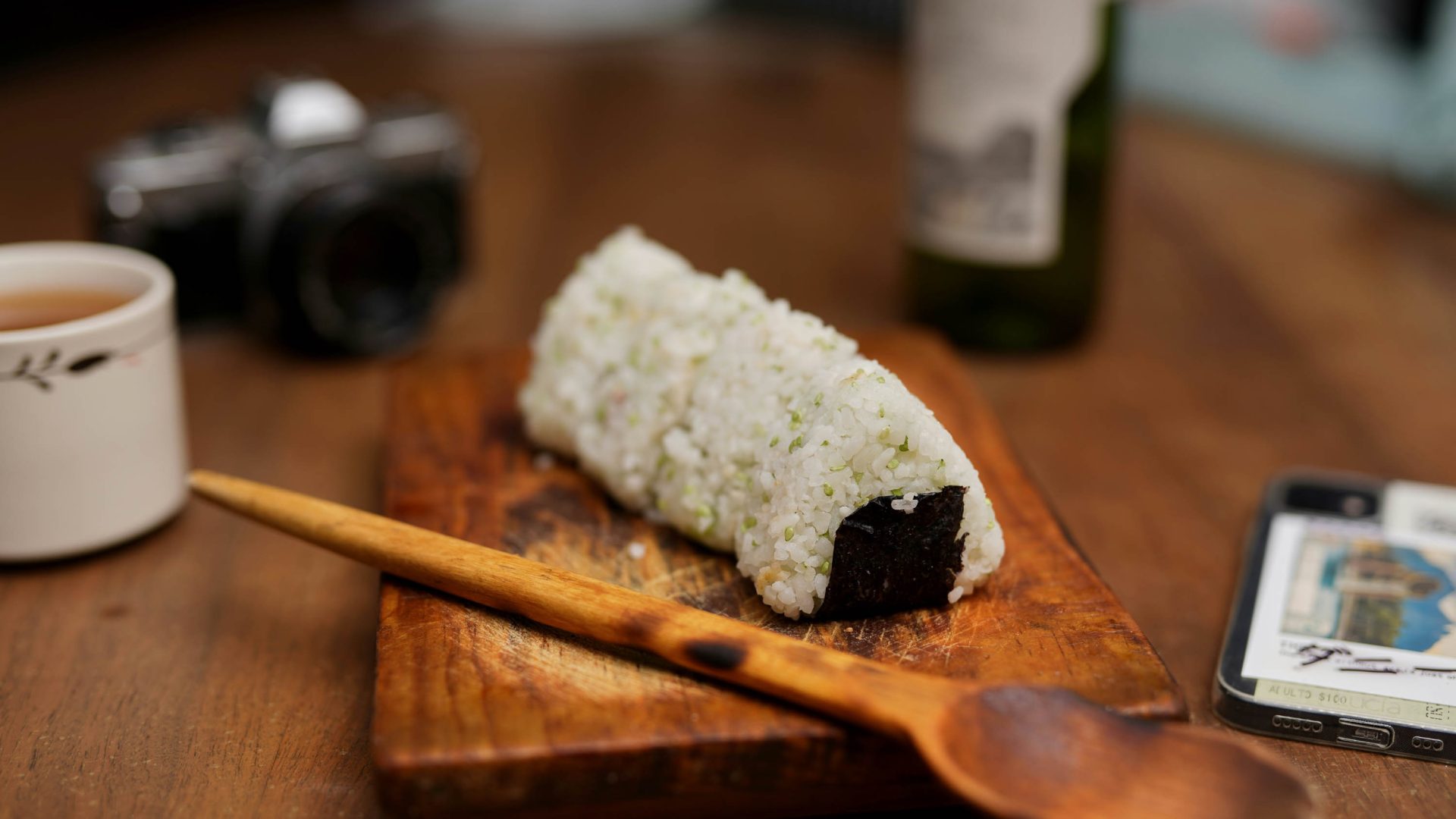 A tray with onigiri on it, alongside a wooden spoon, bottle and camera.