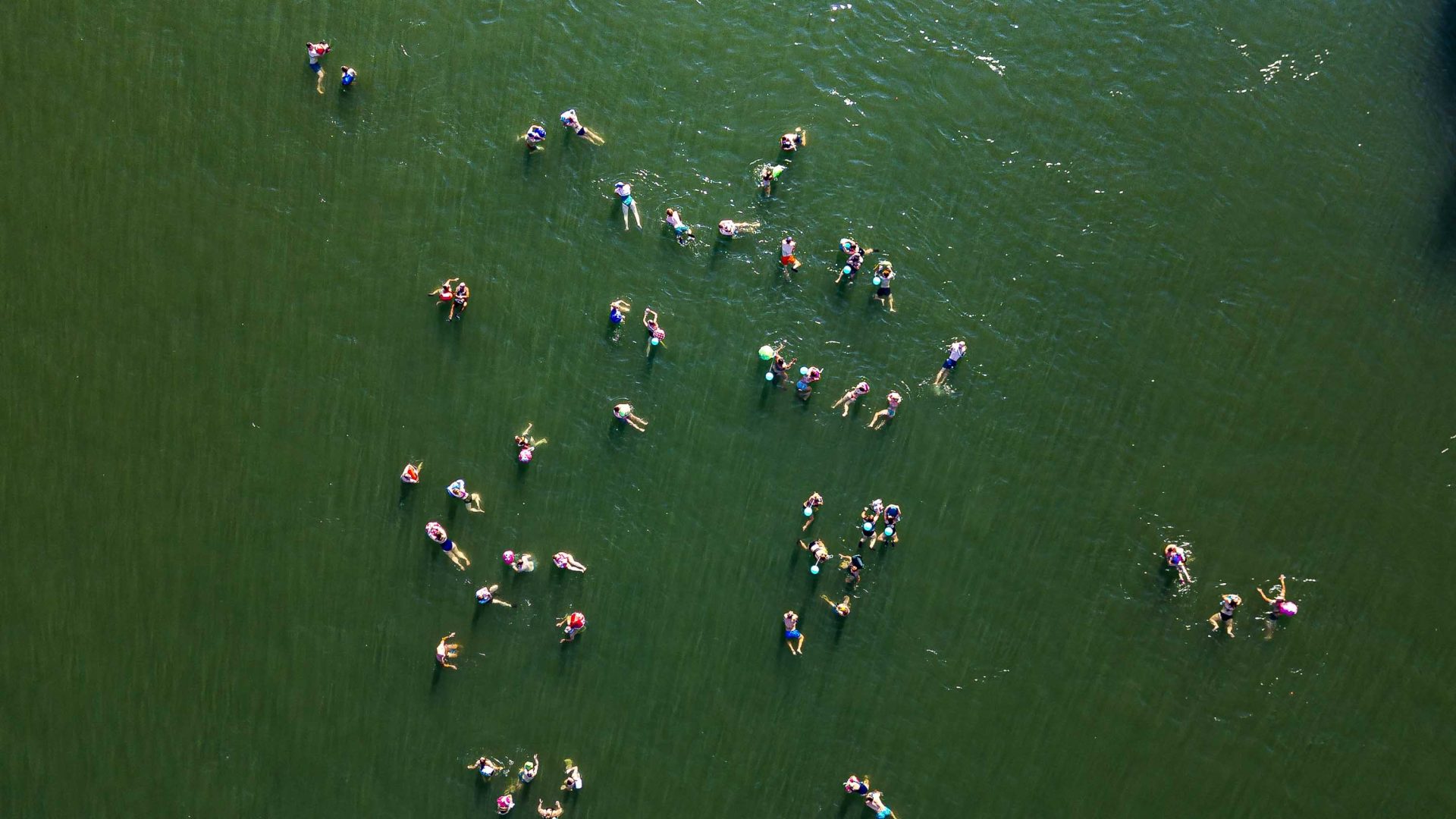 A drone photo of a lot of people swimming in a river and on floaties.