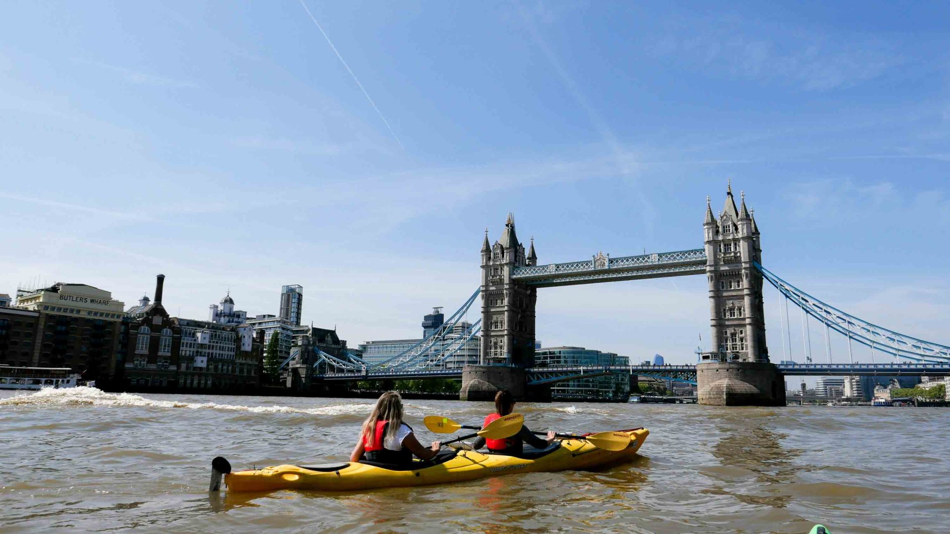 Two kayakers paddle toward Tower Bridge with their backs to the camera.