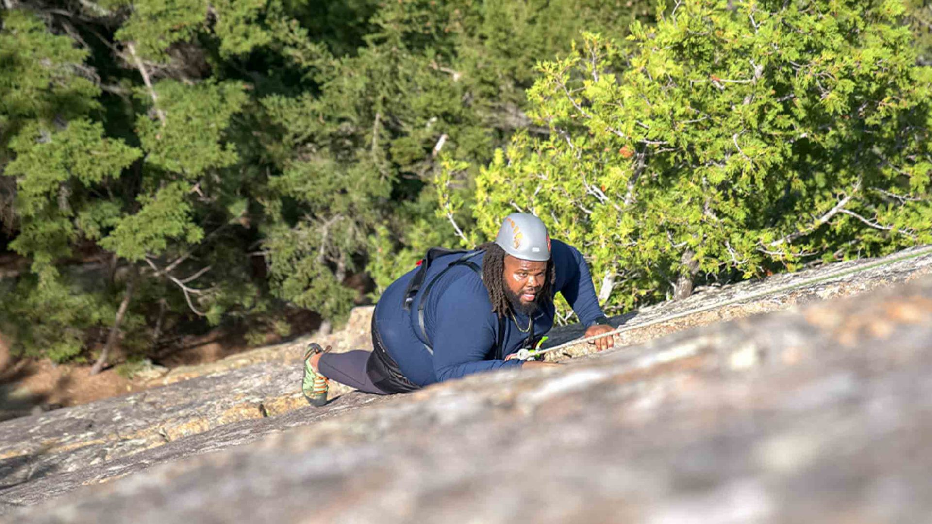 A man in climbing gear and helmet is seen scaling a rock face.