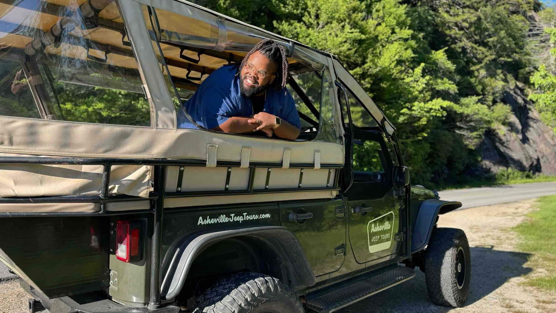 A man leans out the window of a jeep and smiles.