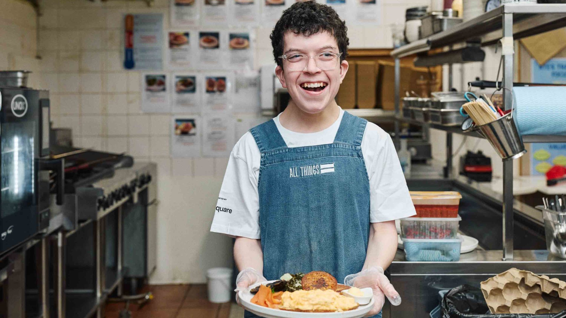 A man holds a plate of food in an industrial kitchen.