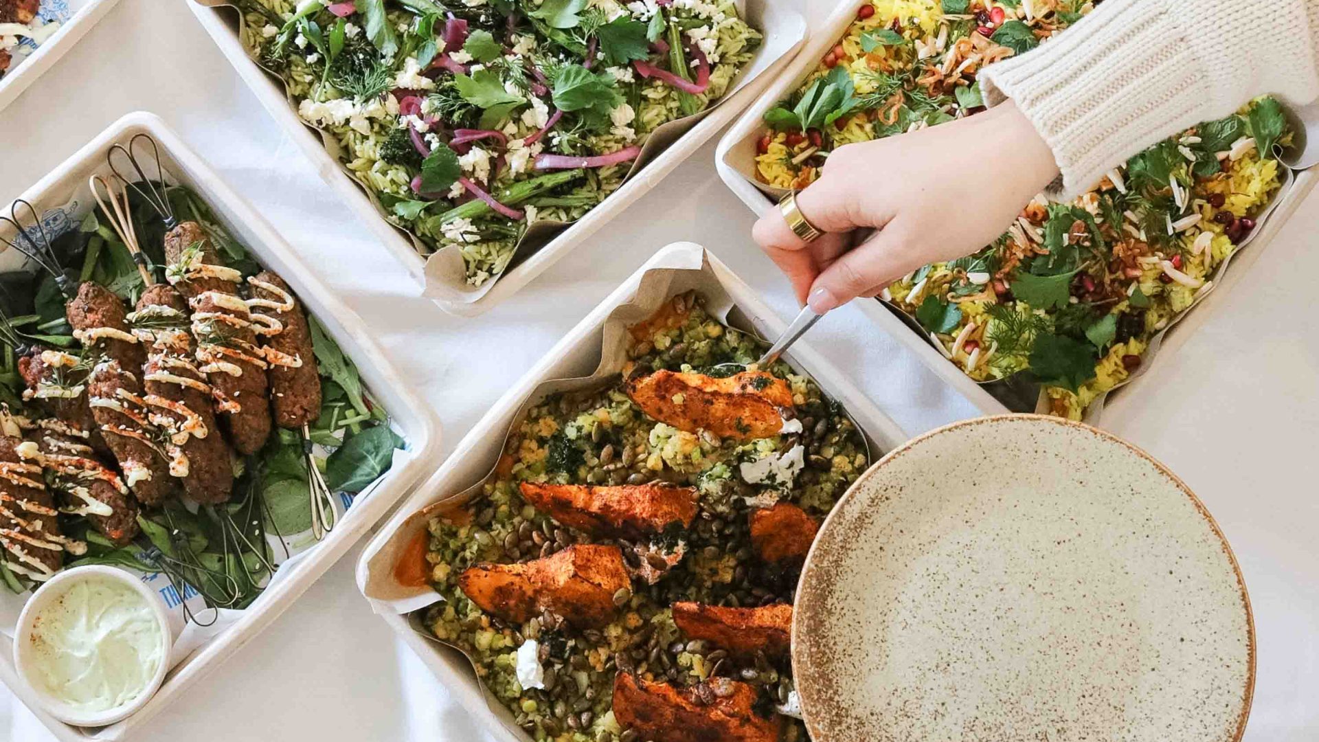 A hand is seen serving up from a dish of food that is alongside other dishes of food.
