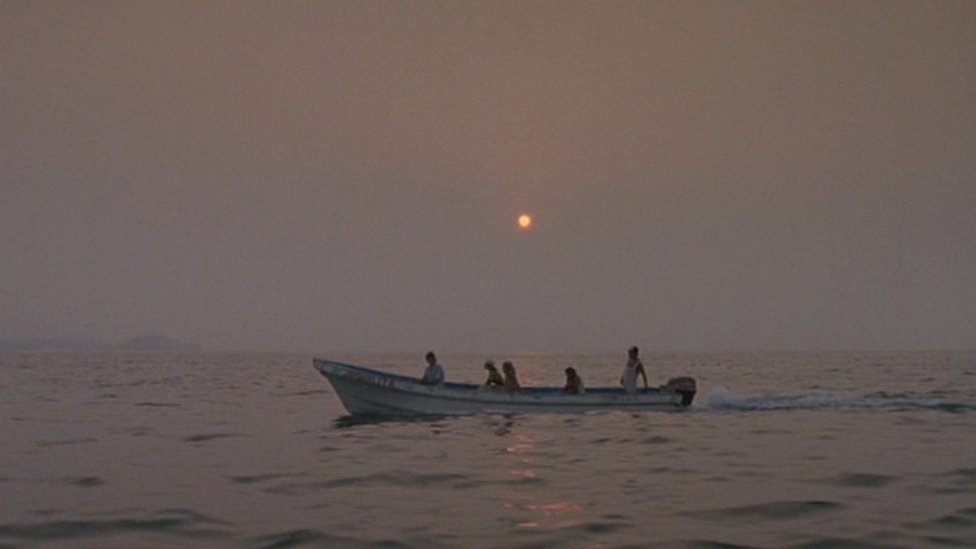 A speed boat moves across an ocean horizon under a setting sun.