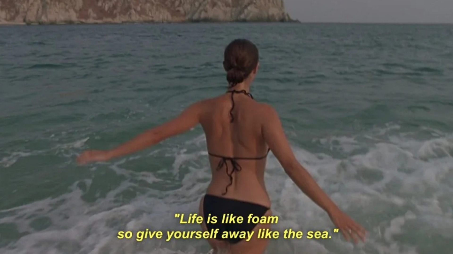 Woman in black bikini walks into ocean.