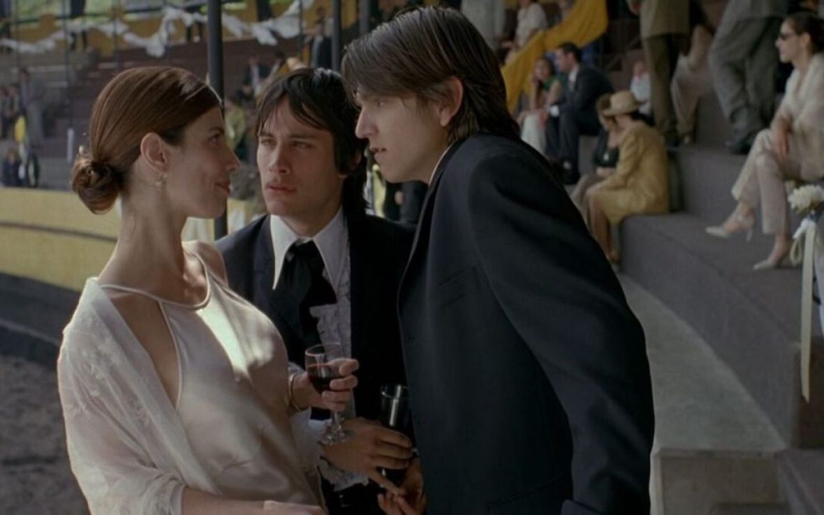 Two men in suits speak to a woman wearing white