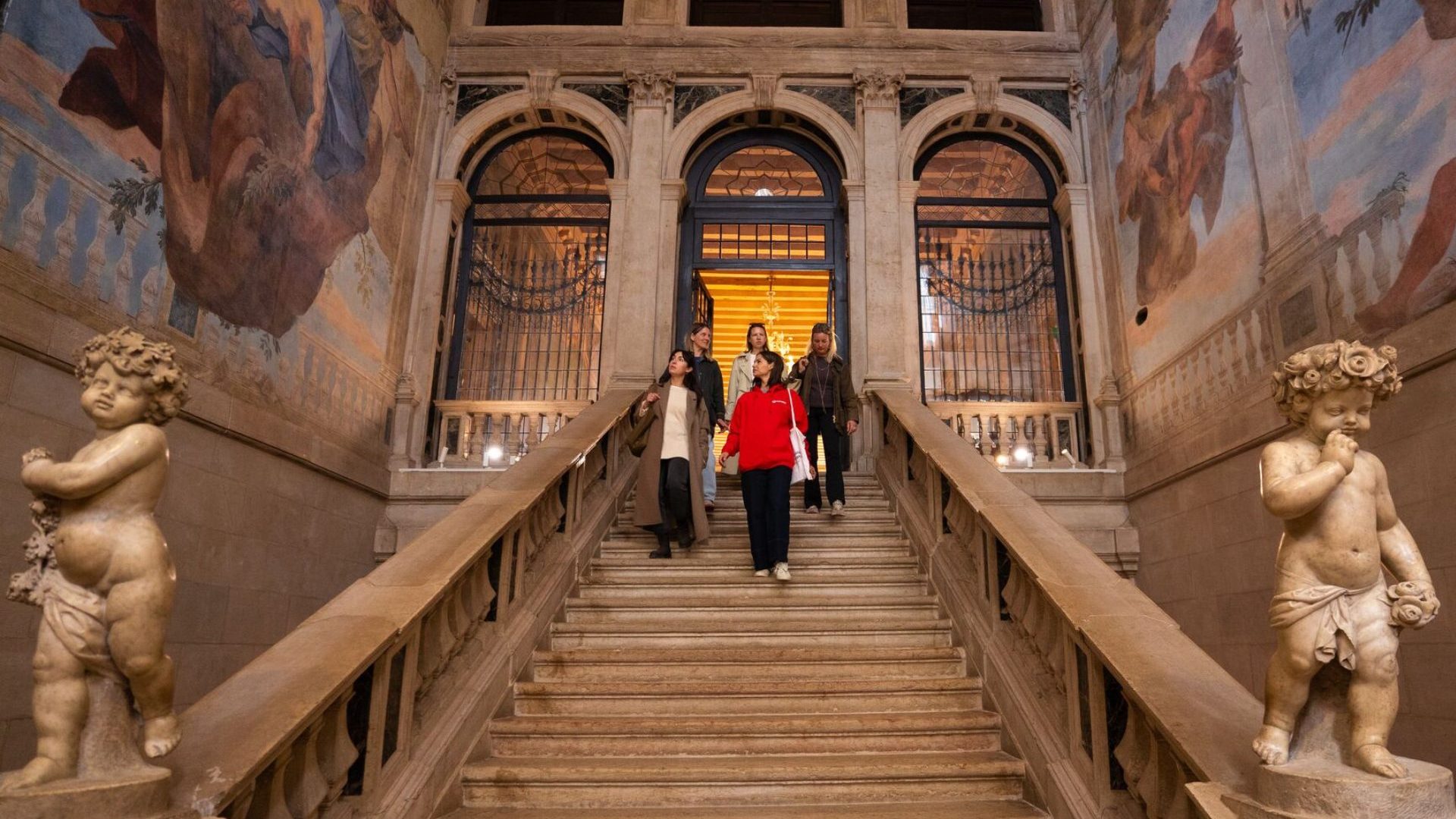 Group walk down stairs beneath painted frescoes