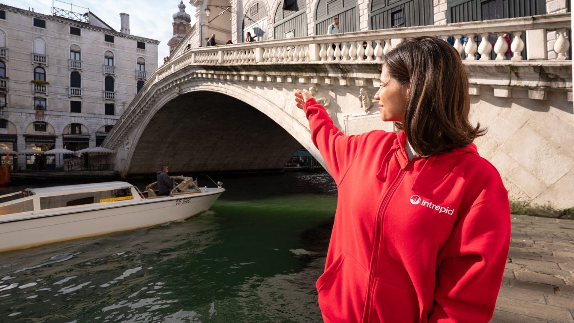Woman in red sweater points at bridge over canal