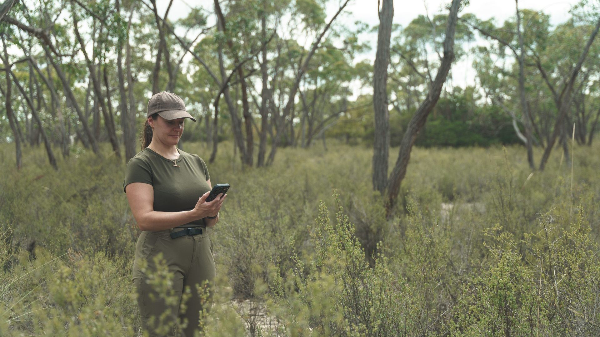 Woman wearing green stands in green waist high bushland.