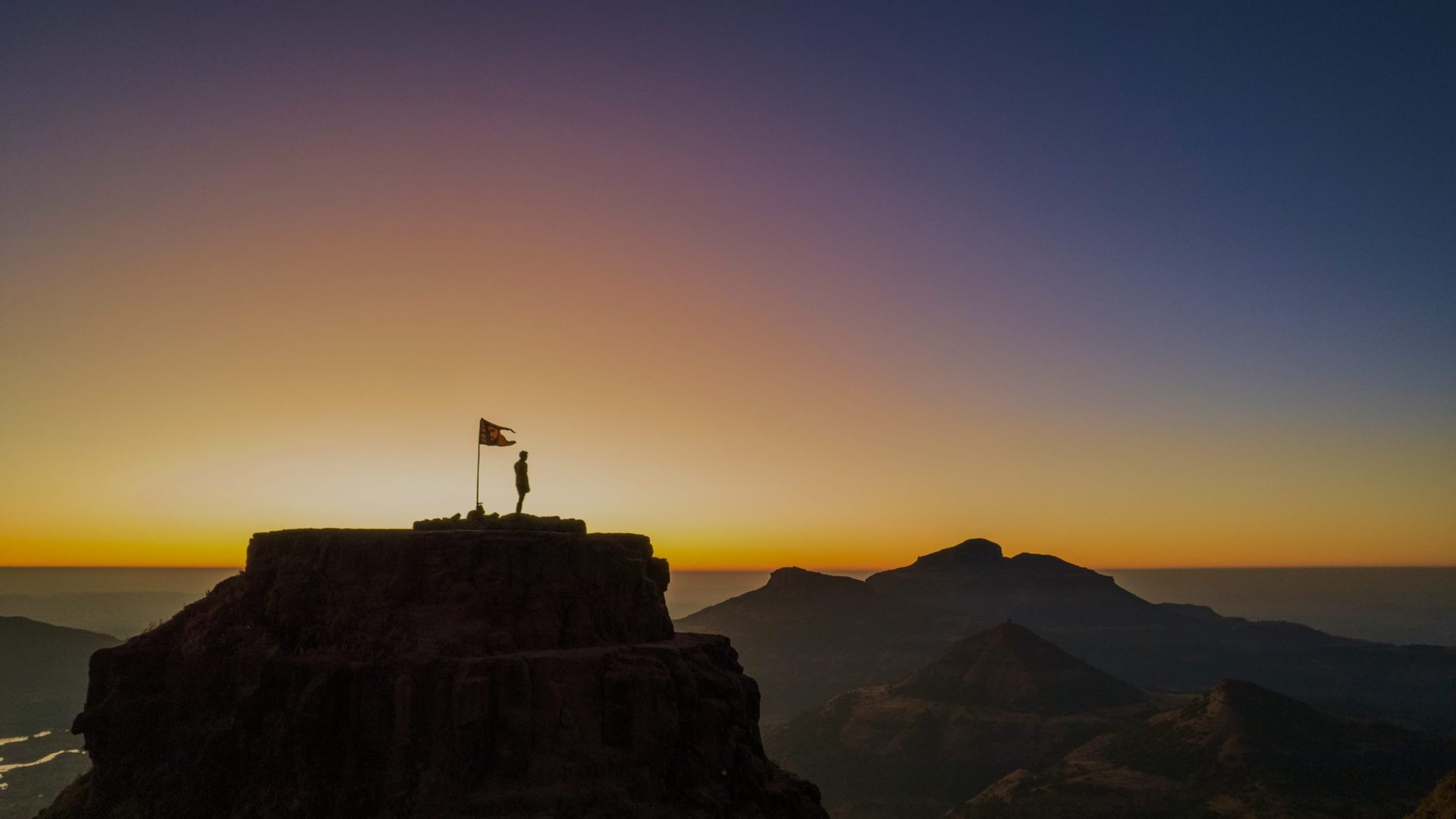 Silhoutte of flag on mountain top against pink sunset.