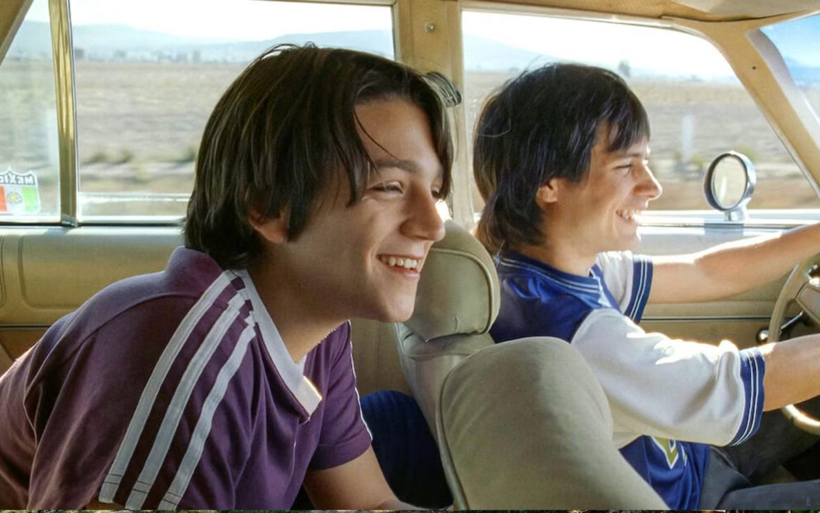 Two boys sit inside a car laughing.