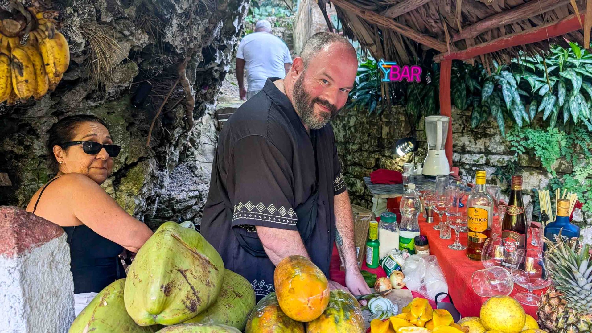 A man smiles as he prepares food at an outdoors location.