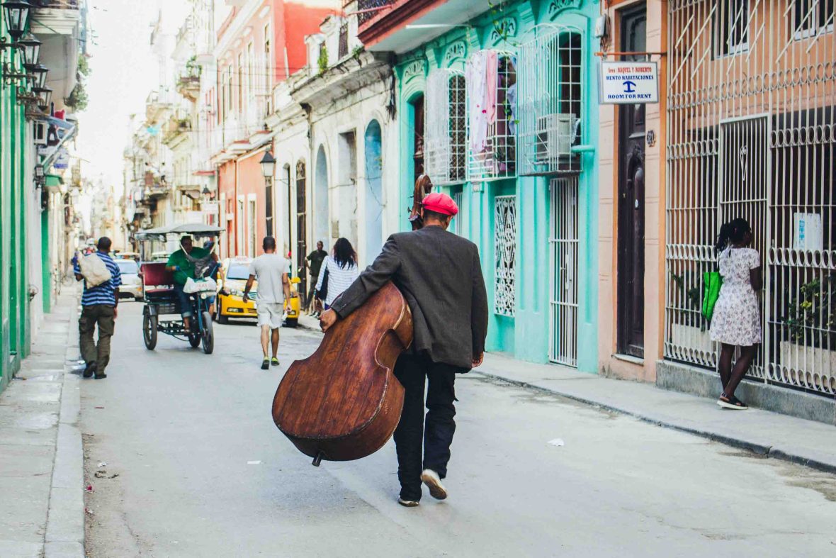 A musician walks with his chello through the coloured street of Havana.