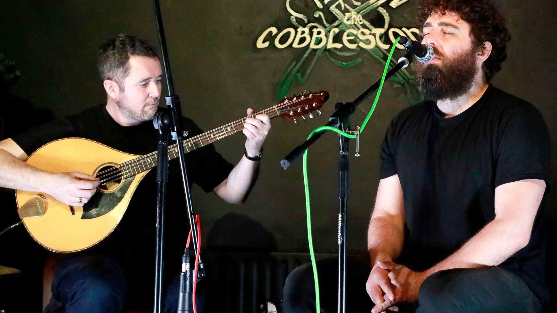 Two men perform on a black stage with the word Cobblestone behind them.