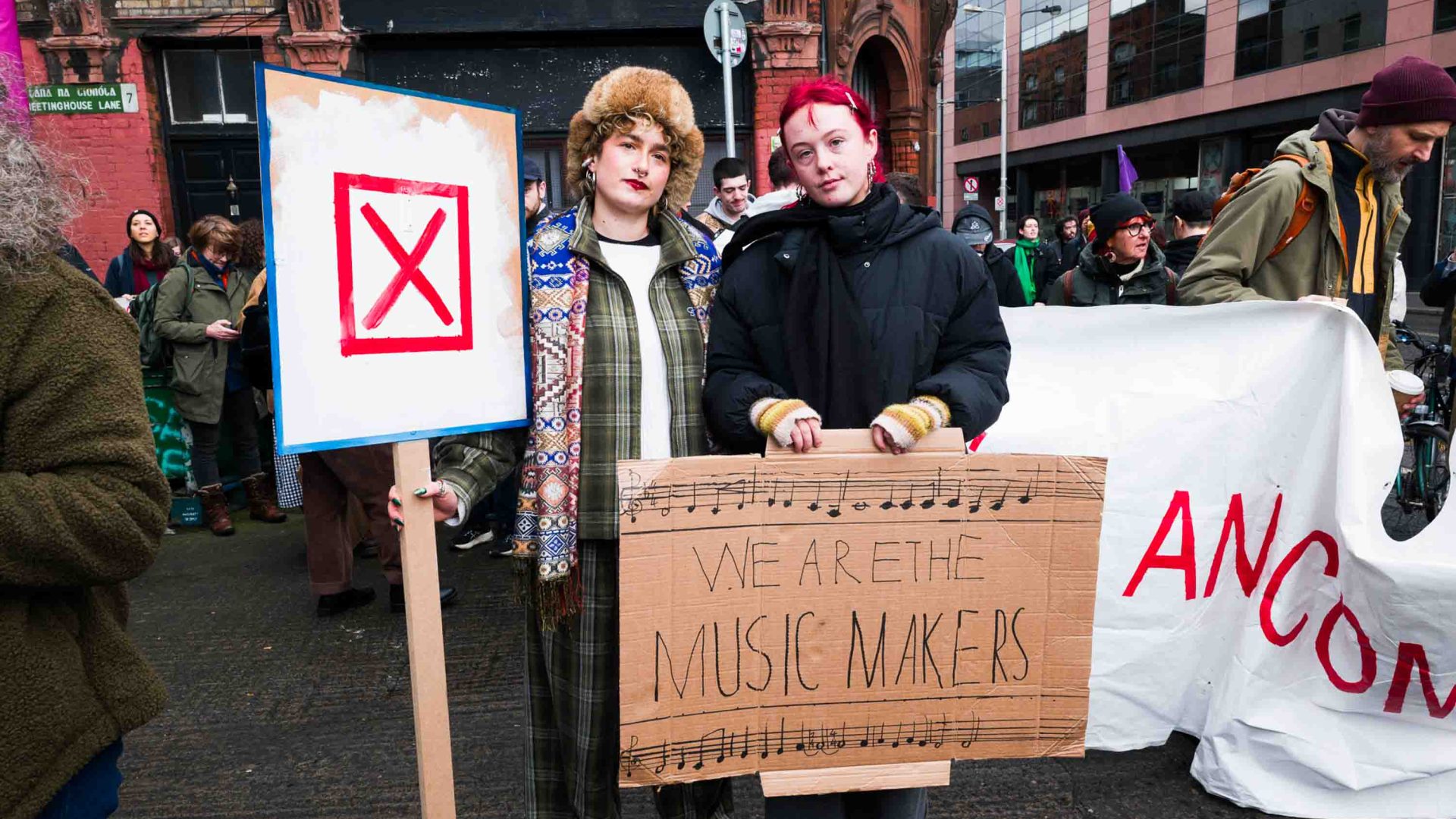 Two protestors pose for a photo with their placards. One reads "We are the music makers".