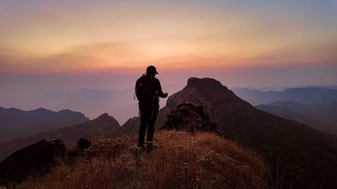 Silhoutte of man on mountaintop against pink sky.