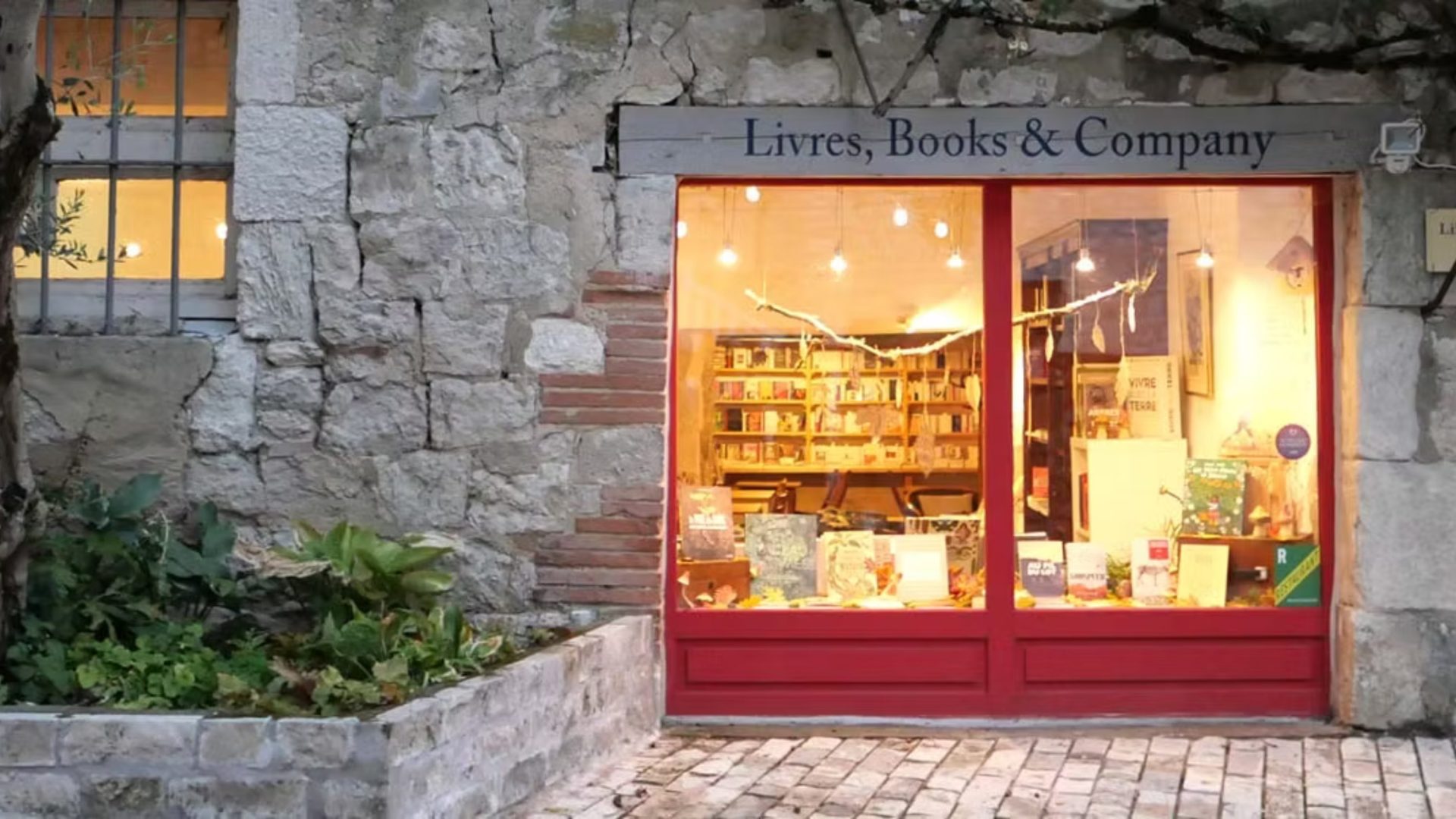 A stone building with red door below a sign reading 'Livres, Books & Company'.