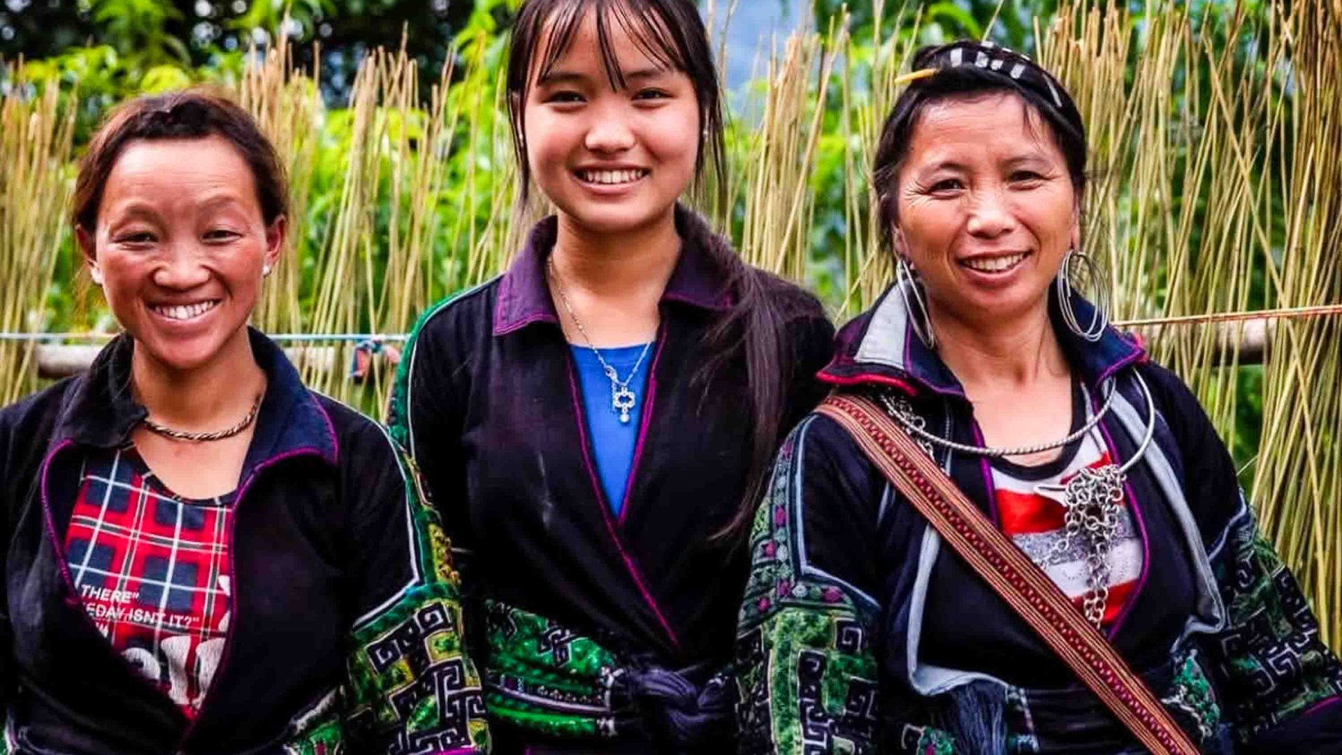 Three women in traditional H’mông clothing smile for a photo.