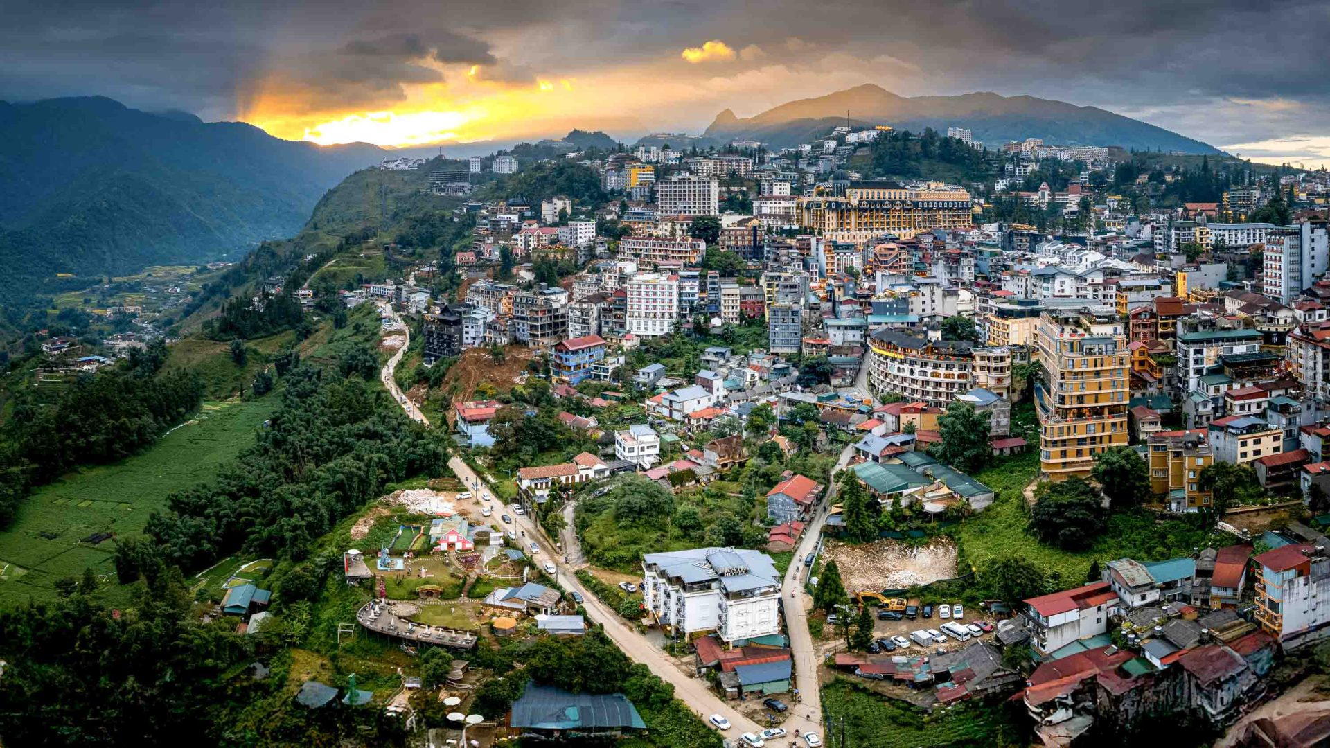 A town on the edge of hills, against a setting sun.