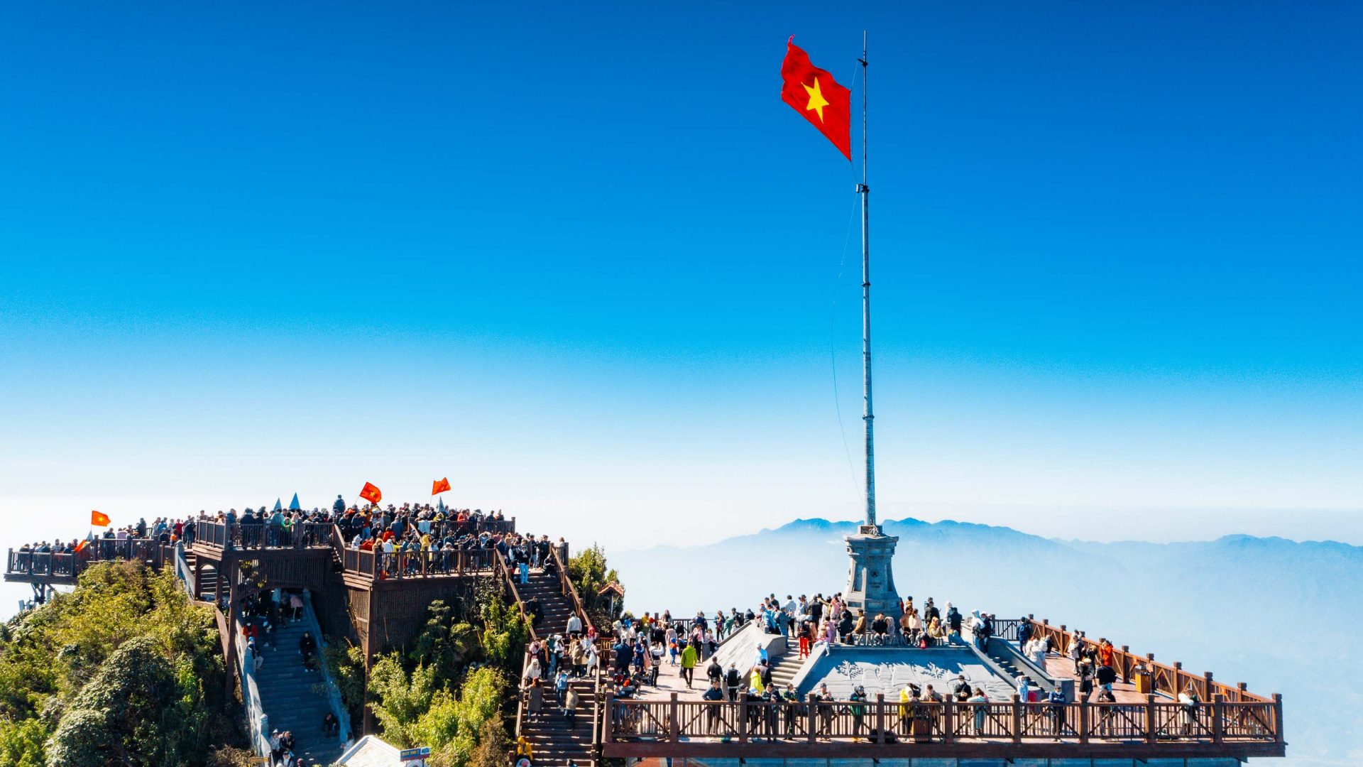 Throngs of tourist on a lookout that has a Vietnamese flag flying above it.