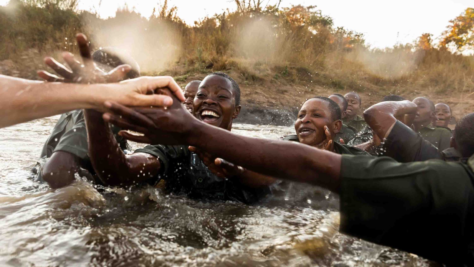 A number of female rangers look happy in a waterhole pumping fists with one another.