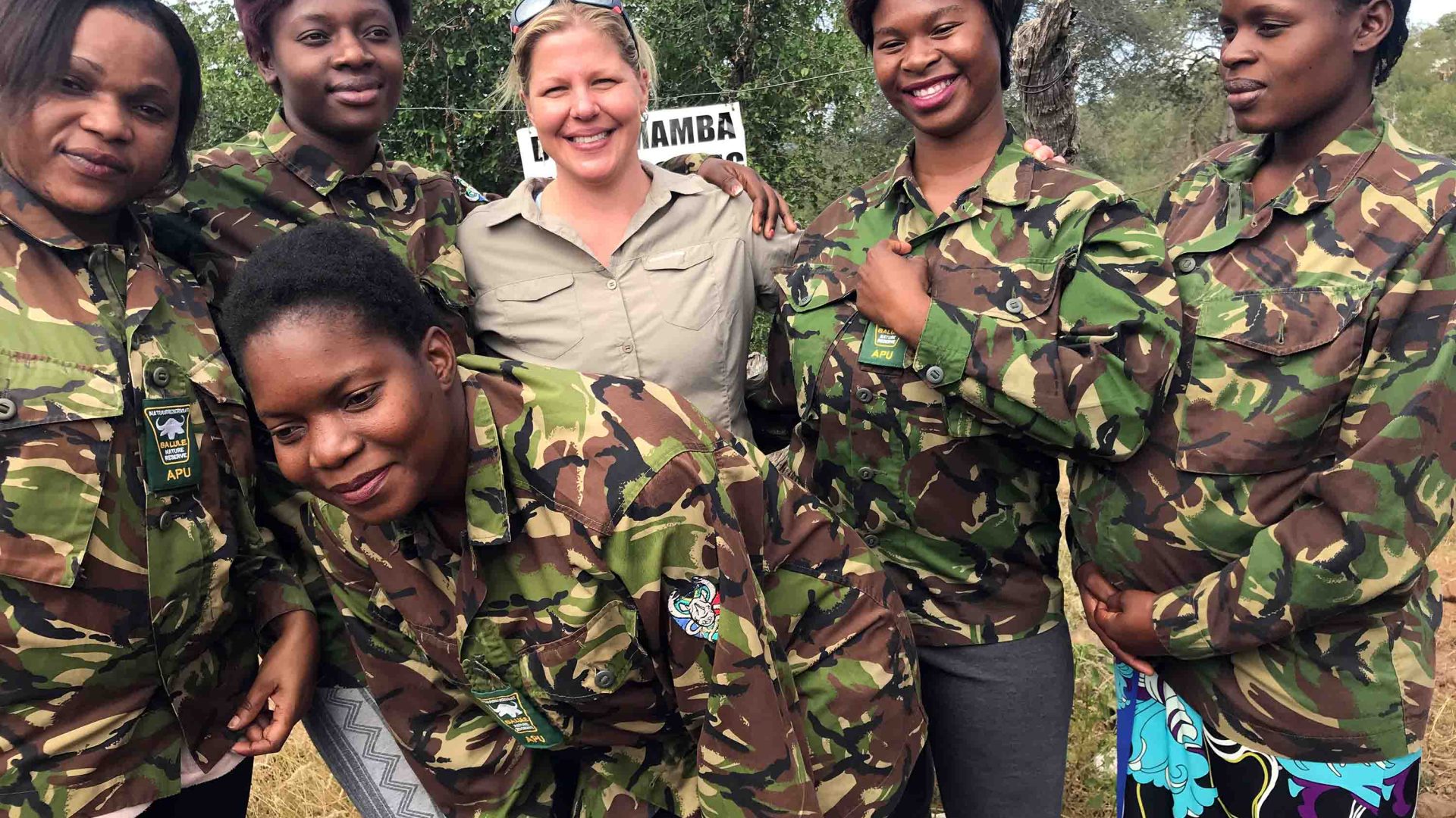 A woman smiles, surrounded by an all female group in army style fatigues.