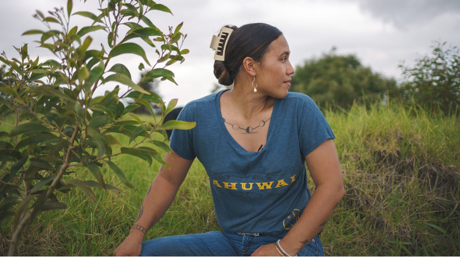 Women wearing blue t-shirt sits beside sapling.