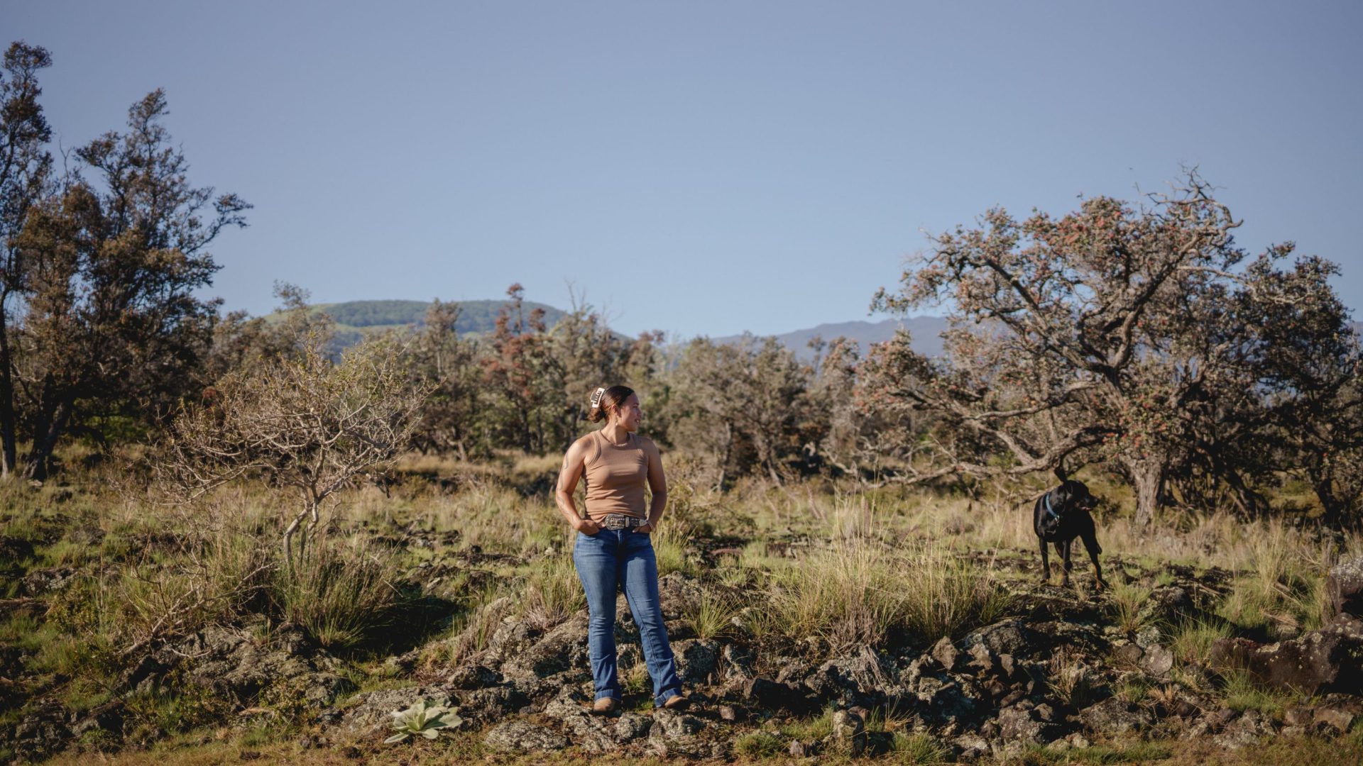 Woman and black dog stand on black volcanic rock.