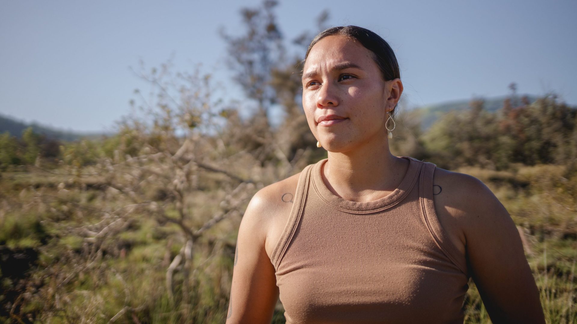 Woman wearing brown tank top looks out into the distance.