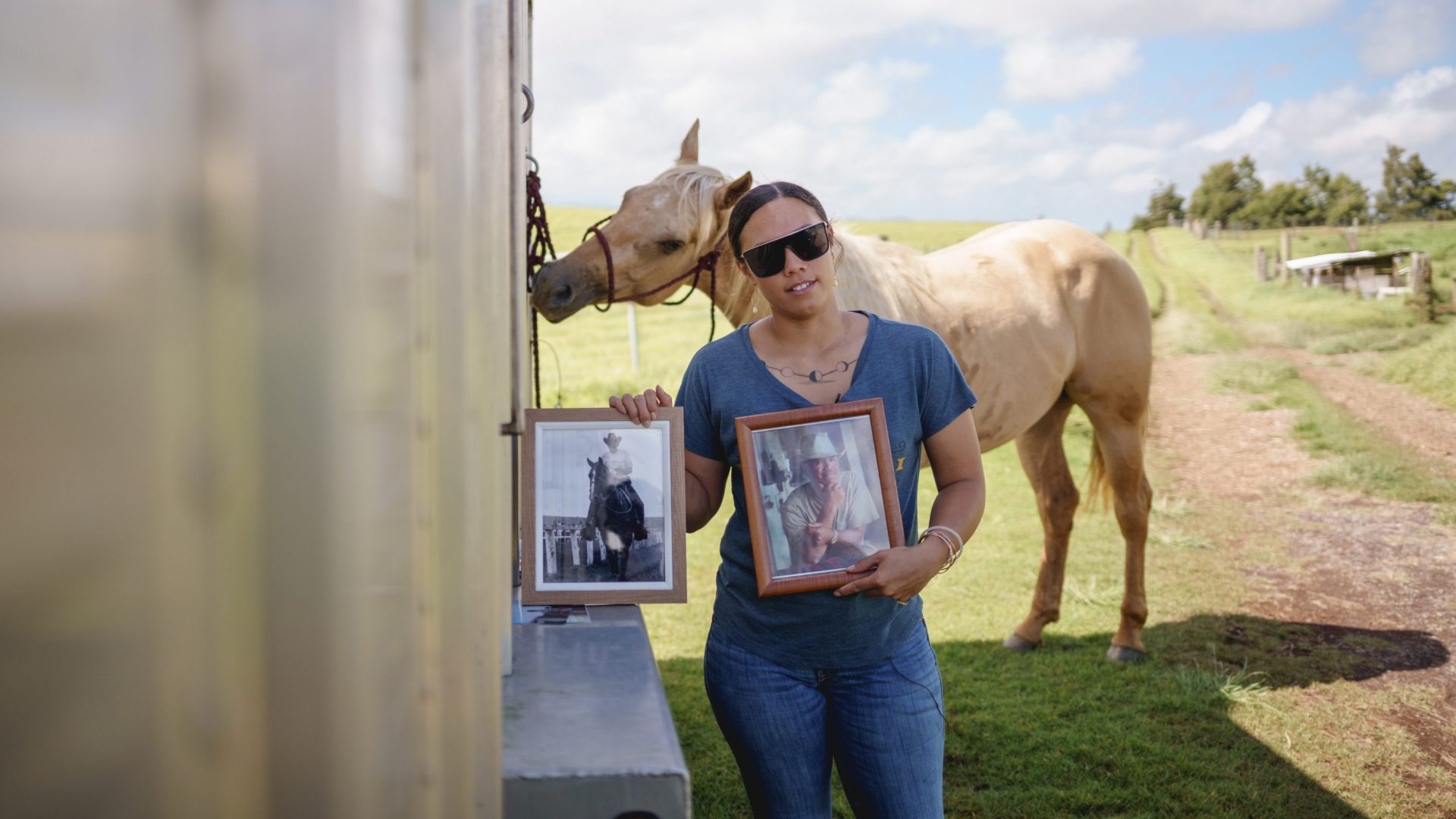 Woman wearing sunglasses stands in front of horse and holds family photos.