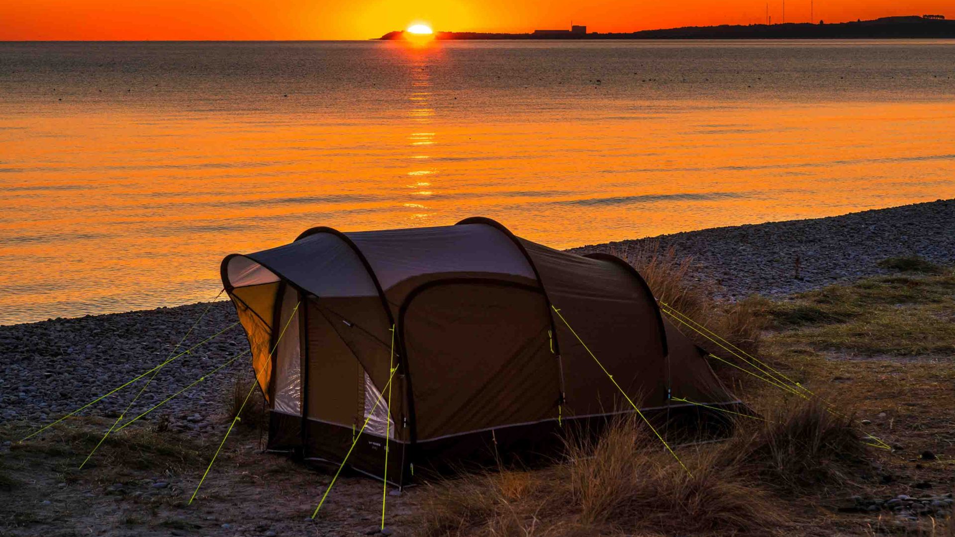 A tent on a beach at sunset.