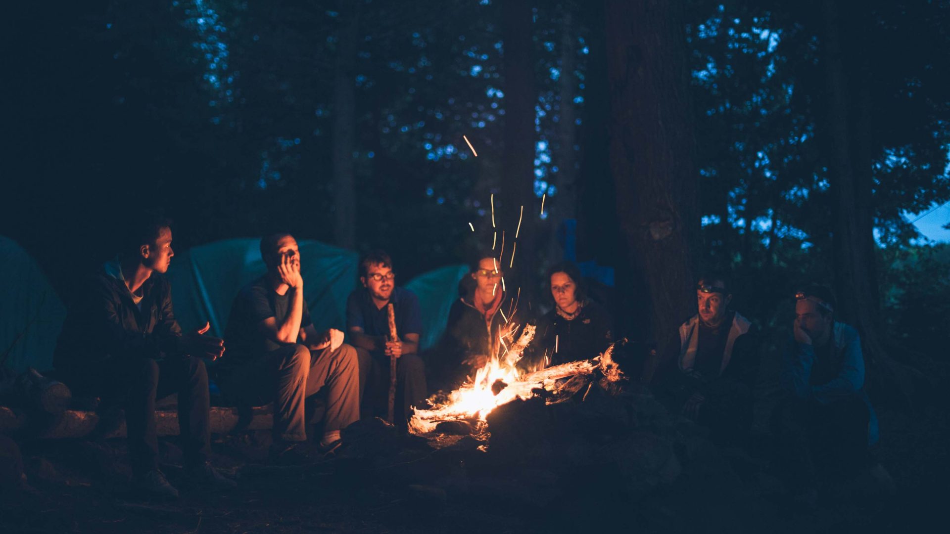 A group of people sit around a campfire at night.