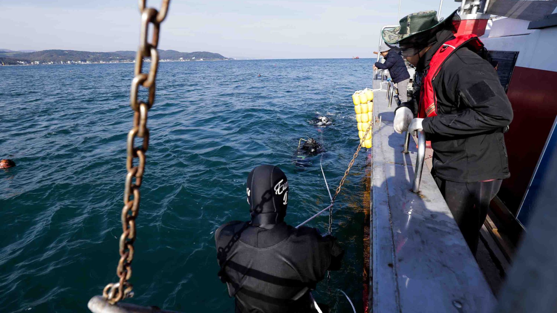 Two divers descend from a boat to the water.