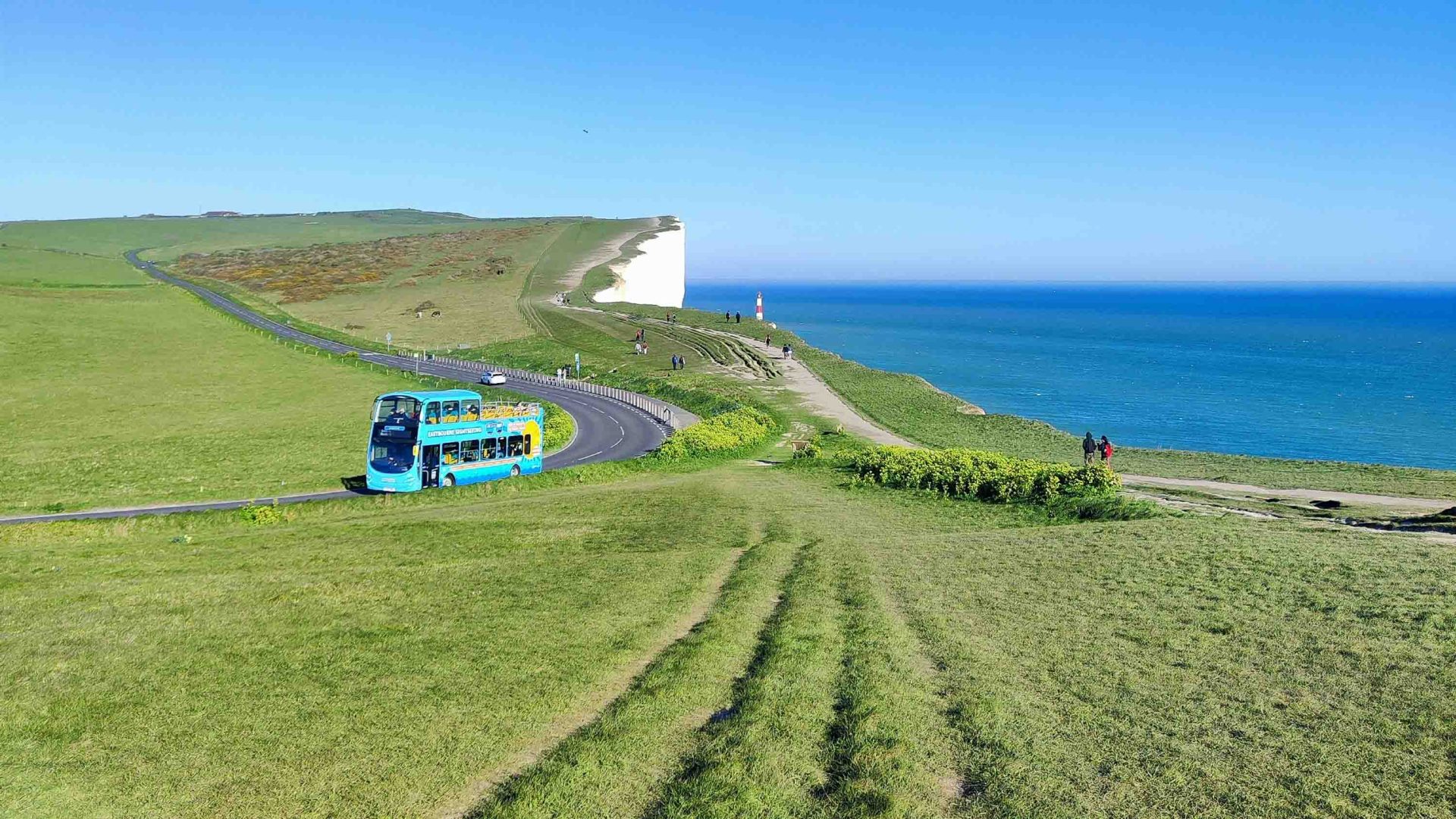 An open roof bus drives along a road by the ocean.