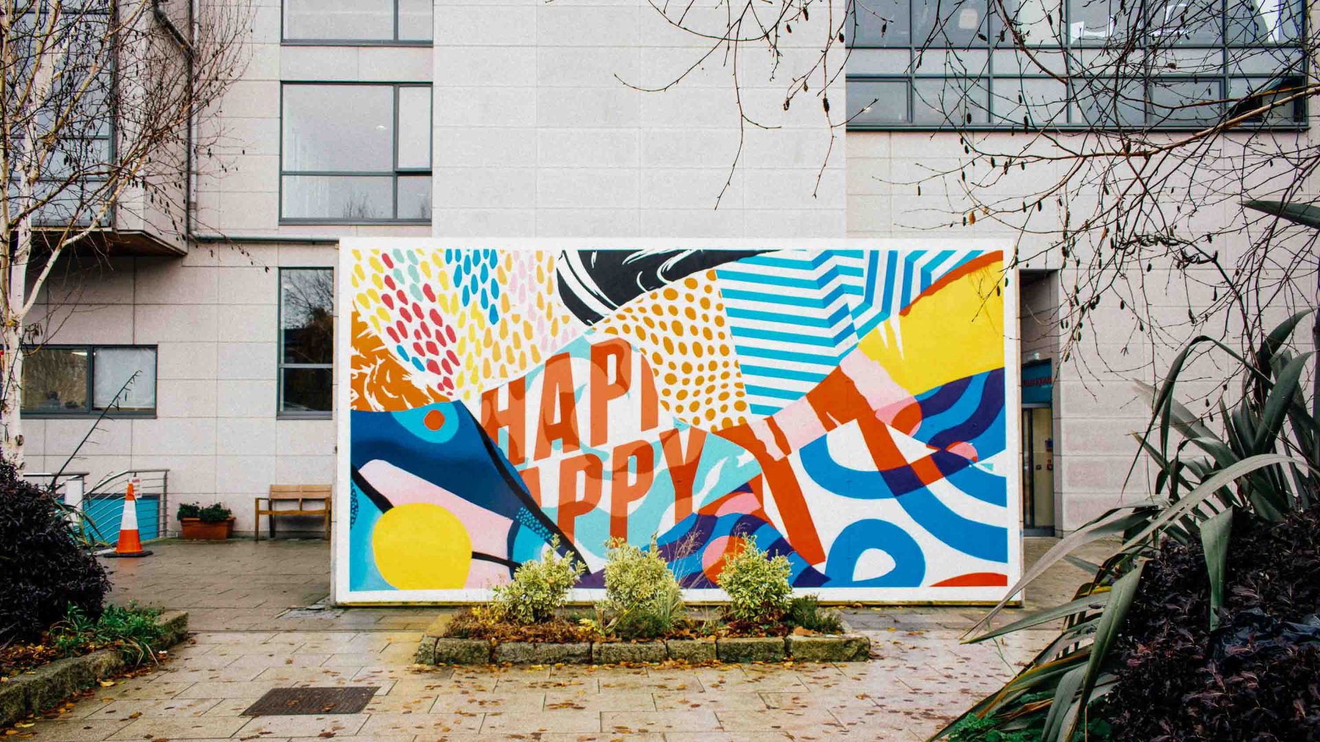 A colourful painting in a courtyard that has the words Happy in it.